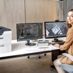 Lachende vrouw in een kantoor naast de Xerox® VersaLink® C620 kleurenprinter
