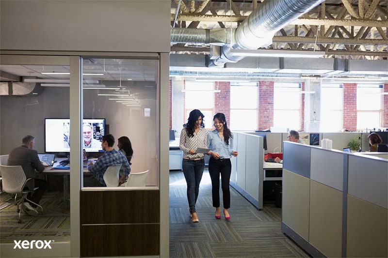 Twee vrouwen lopen door een moderne open kantoorruimte, in gesprek en omringd door werkstations. Twee vrouwen lopen door een moderne open kantoorruimte, in gesprek en omringd door werkstations.